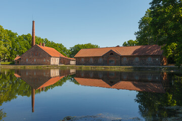An old Olustvere manor in the summer time. The manor's vodka factory buildings are reflected in the...