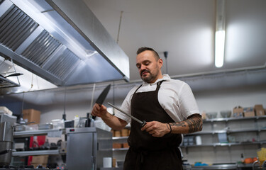 Low angle view of professional chef sharpening knife in restaurant kitchen.