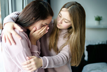 Teenage girl consoling her sad friend on her bedroom
