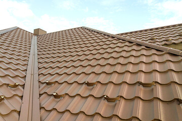 Detail view of house rooftop covered with brown metal tile sheets.