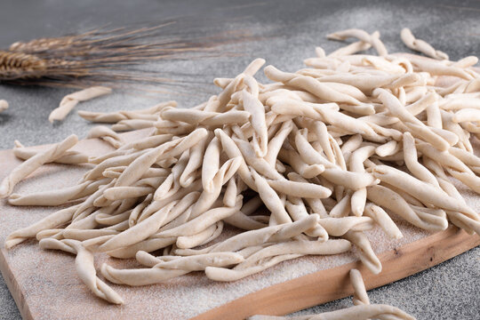 Whole grain wheat apulian pasta Pizzarieddi or maccaruni on a cutting board on black table. Fresh maccheroni typical dish of Puglia, Salento Italy. Italian homemade pasta background