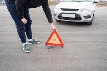 male driver puts red triangle warning sign on the road as the symbol of car accident