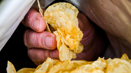 Mans hand is picking potato chips from bag inside view