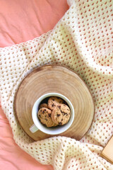 Mug filled with chocolate chip cookies and soft knitted blanket on a bed. Flat lay.