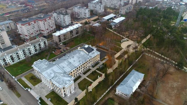 Large palace of culture building in park with bare trees in dwelling city district on gloomy autumn day aerial view