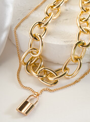 Fototapeta na wymiar Fashion bijouterie - double gold chain with a lock on a white stand