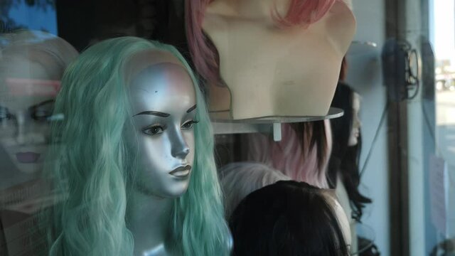 Mannequin head with green hair. Store front window in wig shop. Handheld shot with stabilized camera.