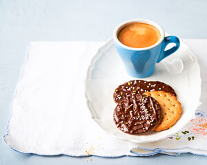Chocolate cookies with colorful sprinkles and coffee for brunch or breakfast on light blue background.