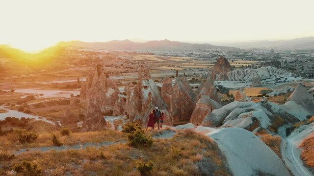 WANDERLUST CONCEPT Drone flies fast around happy family with kids enjoying epic sunset in Cappadocia mountain scenery.