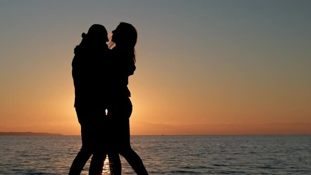 Silhouette of young couple kissing and hugging against sea and sunset