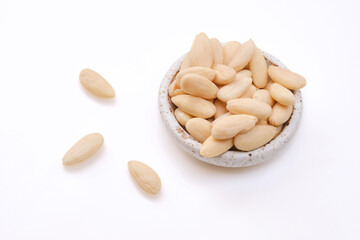 White bowl of peeled or blanched whole almonds on a white background. Shallow depth of field