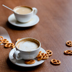 2 cups of coffee latte in a cafe on a wooden table with pretzels