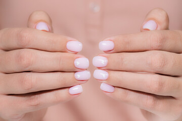 Closeup view photography of beautiful female hands with modern trendy gel polished rounded nails painted with two colors in pink pastel nude look color with cute white small hearts on two nails