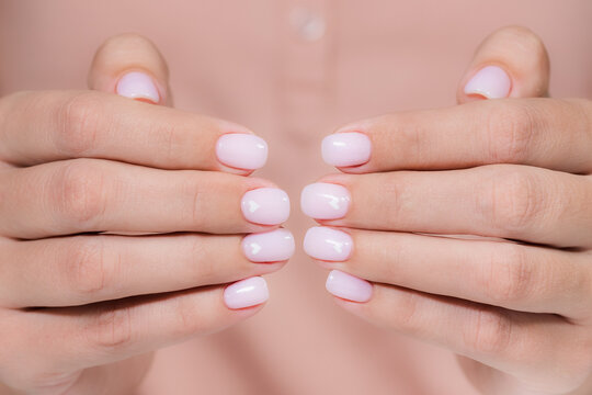 Closeup view photography of beautiful female hands with modern trendy gel polished rounded nails painted with two colors in pink pastel nude look color with cute white small hearts on two nails