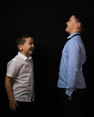 two boys on a black background are brothers.In a white and blue shirt. they look at each other