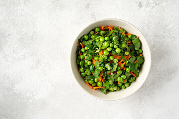 A bowl of salad with green peas, pickled carrots and parsley with olive oil on a bright kitchen table. Delicious healthy salad for health and weight loss. Top view	