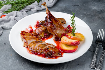 Duck leg confit with berry sauce on white plate on grey table
