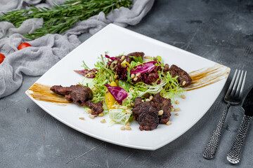 Salad with chicken liver and citrus on white plate on grey table