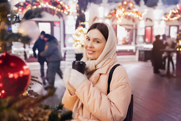 Fototapeta na wymiar Christmas market, portrait woman with cup hot coffee with bokeh light evening. Winter vacations in Red square Moscow, Russia