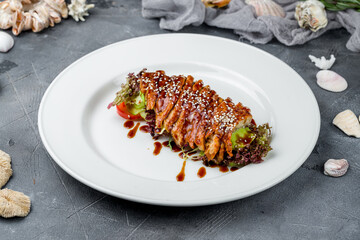 Sashimi eel on a plate with greens on grey table
