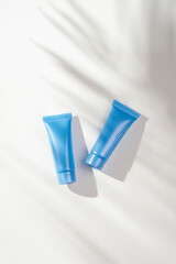 Plastic blue bottles for cream or lotion on a white background. Skin care cosmetic with beautiful palm shadows. Beauty concept for face body care. Place for text