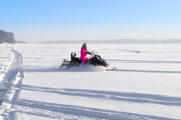 A girl rides a snowmobile through a snow-covered frozen lake. Riding on winter modes of transport....