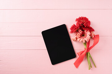 Red gerbera daisy flowers and digital tablet on pink wooden table
