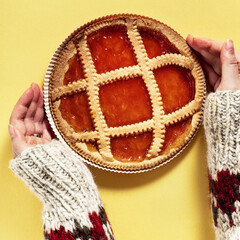 italian crostat pie with apricot jam on a yellow background and female hands in a warm woolen sweater with an ornament