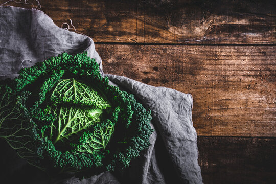 vista superior de una col rizada, col de Saboya o col de Mil&aacute;n sobre un trapo de lino en una mesa de madera vieja con espacio en blanco