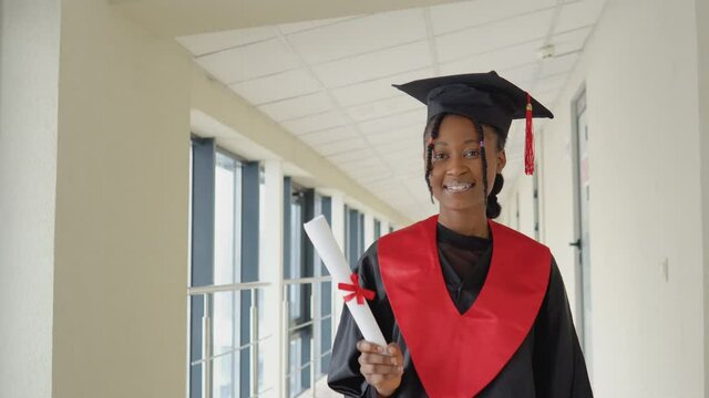 African american female graduate in mantle stands with a diploma in her hands and smiles. A graduate of a medical university with a diploma