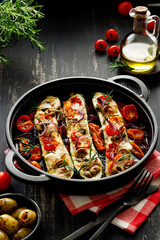 Baked courgettes, zucchini stuffed with goat cheese and vegetables, sprinkled with herbs in a cast iron baking dish on a black wooden table