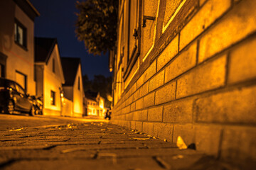 Nachtaufnahme von beleuchteter Straße im Dorf, Gemäuer im Fokus im Vordergrund