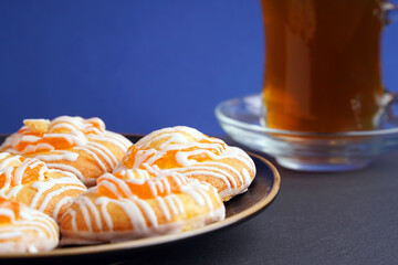 Round biscuits with orange jam on a plate next to a glass of tea on a blue background