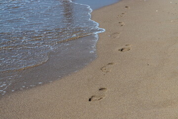 Footprints of a man on the yellow beach sand from walking barefoot by the sea with water that washes away the footprints.
