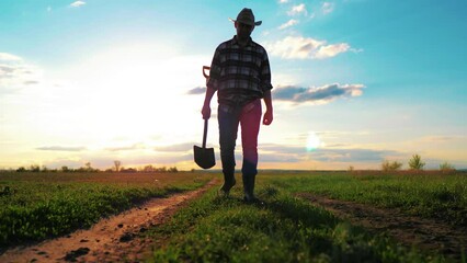 Agriculture concept. Silhouette of a man with a shovel. A tired peasant walks across the field after hard work. Worker agronomist with a shovel goes to sunset. Work on agricultural land concept.