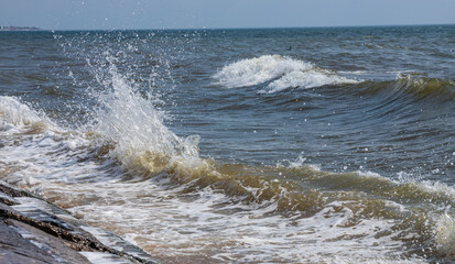 Sea waves crash against large rocks on the shore, forming large splashes