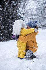 Fototapeta na wymiar Happy hugging children in winter park. Falling snowflakes. Brother and sister in yellow jackets hug