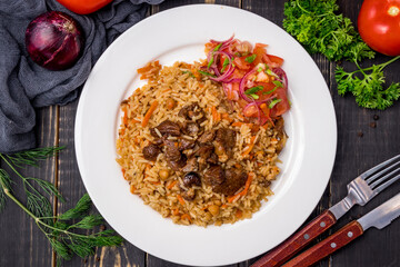 pilaf with beef and vegettables salad on white plate on dark table top view