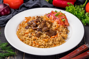 pilaf with beef and vegettables salad on white plate on dark table