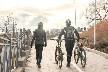 cyclists lead bicycles uphill. Man and woman on the background of a cloudy sky. View from the back
