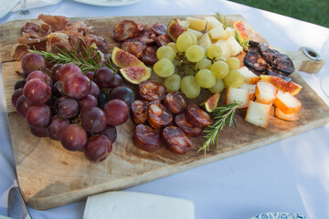 Delicious assorted snacks on a wooden cutting board. Ham, grapes, cheese, figs and chorizo.