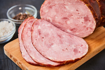 Homemade ham, sliced on a wooden table on a cutting board with spices and salt. Traditional ham homemade, ready to eat, delicious breakfast. The concept of meat products.
