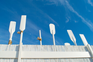 White wooden oars on a white-painted wicker cane fence against a blue sky.