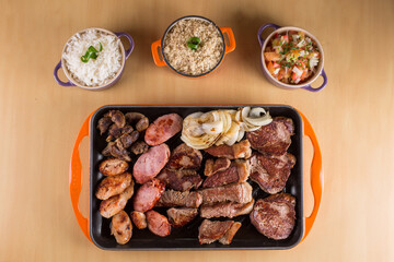 Picanha, a traditional cut of Brazilian meat, served with grilled onion and sausage on a hot iron plate. Brazilian barbecue served on a hot iron plate accompanied by rice, farofa and vinaigrette sauce