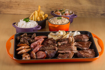 Picanha, a traditional cut of Brazilian meat, served with grilled onion and sausage on a hot iron plate. Brazilian barbecue served on a hot iron plate accompanied by rice, farofa and french fries