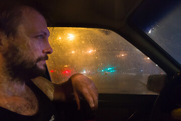 Hombre esperando dentro del auto a que pare de llover  mientras disfruta mirar la lluvia de verano