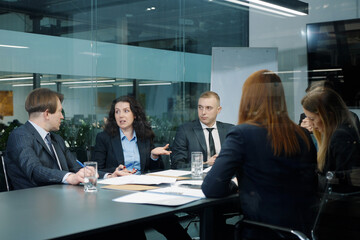Business people in official wear sitting in office behind glass wall and discussing project, colleagues sharing ideas, teamwork of managers brainstorming, executives planning strategy