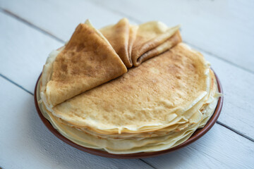 Crepes, thin pancakes on a plate on a white wooden table