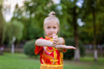 Cute little caucasian girl seven years old in red sport wushu uniform exercising in park at summer...