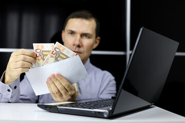 Envelope with euro banknotes in hands of man in office clothes sitting at laptop. Wages, bonus or bribe concept